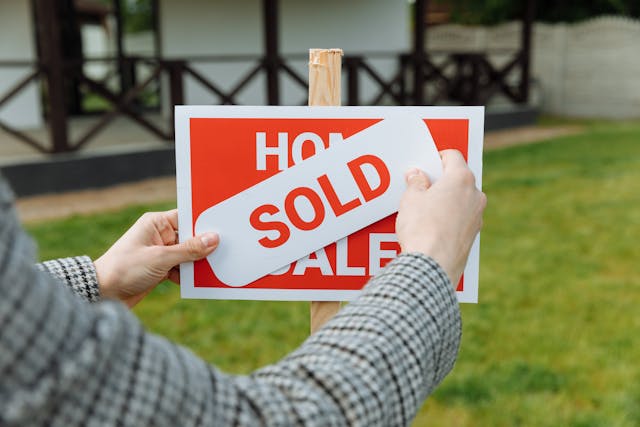 a real estate agent placing a sold sticker over a for sale sign